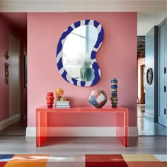 a pink room with a mirror and vase on the table