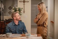 a woman standing next to a man sitting at a table in front of a cross