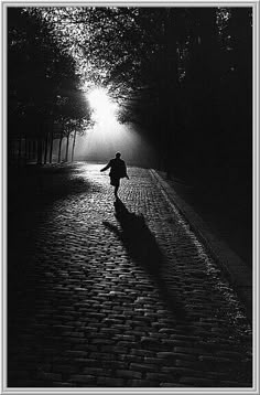 a person walking down a street at night with the sun shining through trees behind them