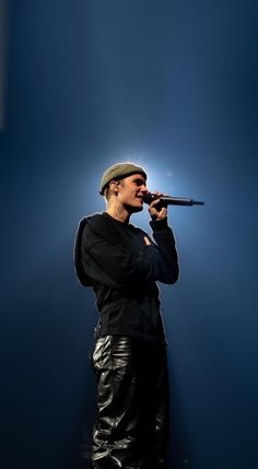 a man in black shirt and leather pants holding a microphone up to his mouth while standing on