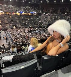 a woman wearing a fur hat sitting in an empty stadium with her hands on her hips