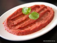 a white plate topped with meat covered in sauce and green leafy garnish