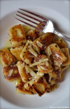 a white plate topped with pasta covered in sauce and onions next to a fork on top of a table