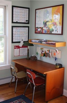 a desk with two chairs next to it in front of a window and pictures on the wall