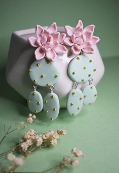 two pink and blue flower earrings sitting on top of a white vase next to flowers