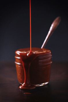 a jar filled with melted chocolate on top of a wooden table next to a spoon