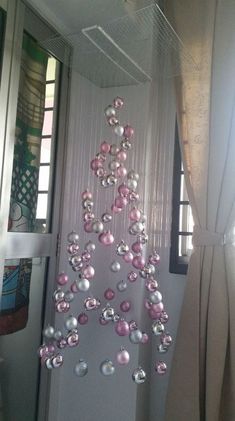 a christmas tree made out of pink and silver ornaments hanging from the ceiling in front of a window