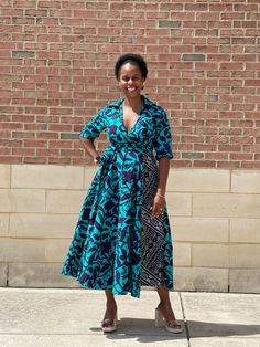 a woman standing in front of a brick wall wearing a blue and black patterned dress