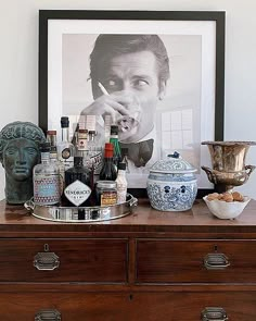 an old dresser with liquor bottles and other items on it next to a framed photograph