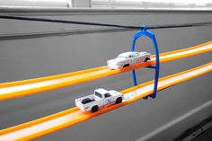 two toy cars are on the track with orange and blue wires attached to it's sides