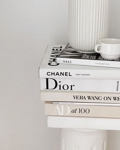 three books stacked on top of each other next to a white vase with a coffee cup