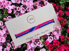 the pink and blue bracelet is laying on top of some purple flowers, which are in front of a white card