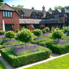 a large brick house surrounded by lush green grass and purple flowers in the front yard