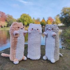 three crocheted cats standing next to each other on top of a rock near water