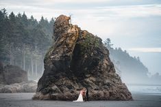 a bride and groom standing in front of a rock formation on the beach near the ocean