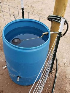 a large blue barrel sitting next to a wooden pole on the ground in front of a fence