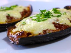 two stuffed eggplant halves covered in cheese and herbs on top of a white plate