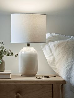 a white lamp sitting on top of a wooden table next to a night stand and bed