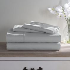 a stack of blue sheets sitting on top of a wooden table next to a vase with white flowers