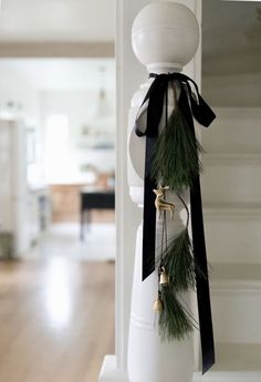 a white vase with black ribbon and bells on the top is decorated with pine branches