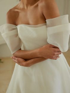 a woman in a white dress is holding her arms crossed and looking off to the side