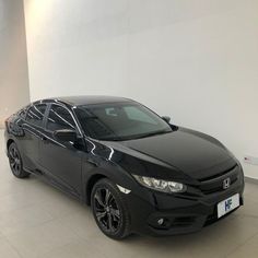 a black honda civic is parked in a room with white walls and tile flooring