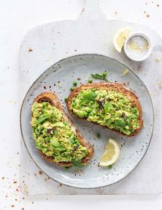 an avocado toast on a plate with lemon wedges