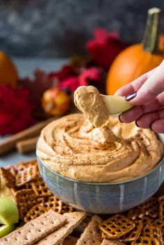 a hand dipping an apple into a bowl of pumpkin spice dip surrounded by crackers