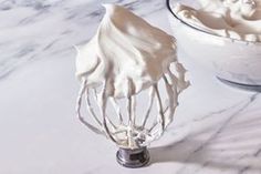 a white bowl filled with whipped cream next to a whisk on top of a counter