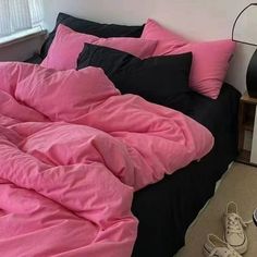 an unmade bed with pink sheets and black comforter in front of a window