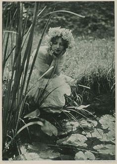 an old photo of a woman sitting on the ground next to some water and plants