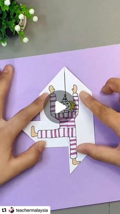 two hands are holding an origami house with a clock on the front and one hand is pointing at it