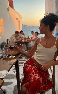 a woman sitting at a table in front of the ocean with people eating and drinking