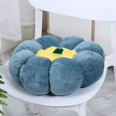 a blue and yellow pillow sitting on top of a white chair next to a potted plant