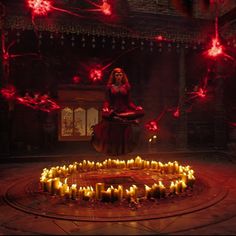 a woman sitting in the middle of a circle of candles with red lights around her