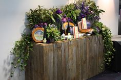 an assortment of cheeses and wine on display in front of a wooden box with greenery