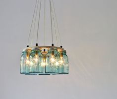 three mason jar chandelier with lights hanging from the ceiling in front of a white wall