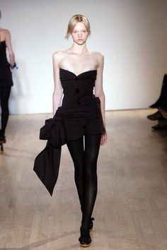 a woman walking down a runway in a black dress and tights with stockings on