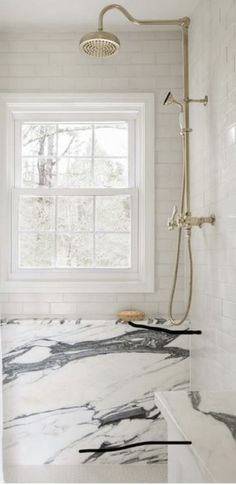 a bathroom with white and black marble counter tops, shower head, and window in the background