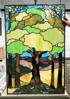 a hand holding up a stained glass window with trees on it and mountains in the background