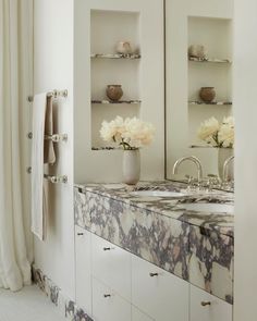 a bathroom with marble counter tops and double sinks in front of open shelves filled with flowers