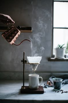 a person pours coffee into a cup with steam rising from it, on a counter