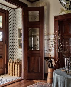 an entryway with wooden doors and baskets on the floor, next to a vase filled with flowers