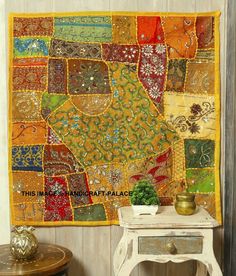 a table with a potted plant on top of it next to a colorful patchwork wall hanging