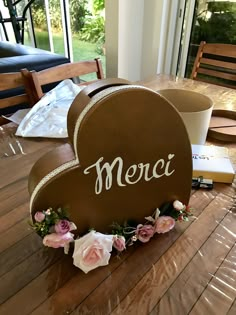 a heart shaped box with the word merci on it sitting on a wooden table