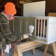 a man in an orange hat spray painting a baby crib