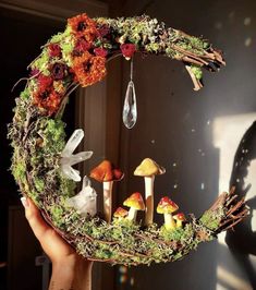 a person holding up a wreath made out of mushrooms and moss with water droplet hanging from it