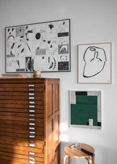 a wooden cabinet sitting next to a wall with pictures on it and a stool in front of it