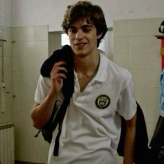 a young man in a white shirt is holding a black backpack and smiling at the camera