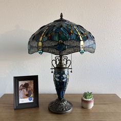 a table lamp with a dragonfly shade on it next to a photo frame and succulents